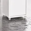 A close-up shot of the bottom of a white cabinet with clear legs, standing on a wet floor. Náhled obrázku produktu
