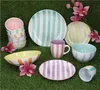 A collection of striped ceramic dishes and mugs arranged on a green grassy surface, with pink flowers. Voir les images du produit