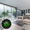 A modern living room with a large window overlooking a courtyard, featuring a sectional sofa, coffee table, and a cannabis-themed clock. Produktbild-Vorschau