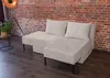 A beige sectional sofa with corduroy texture is placed in a room with a brick wall and wooden floor. A floor lamp and a potted plant are visible in the background. Produktbild-Vorschau