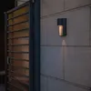 An outdoor wall light illuminates a stone wall next to a wooden gate. Anteprima dell’immagine prodotto