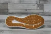 The sole of a white shoe is shown against a background of gray and white wooden planks. Náhľad obrázku produktu