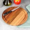 A wooden cutting board with a knife on it, placed on a gray surface with a green cloth and an apple in the background. Voir les images du produit