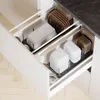 A kitchen drawer organizer containing white storage containers and brown pot lids. Produktbild-Vorschau