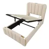 A beige upholstered bed frame with the mattress support mechanism partially raised, revealing storage space underneath. The bed has a padded headboard and footboard with gold accents. Náhled obrázku produktu
