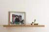 A wooden shadow box frame with a child's photo and decorative pine cones and branches sits on a wooden shelf next to small potted cacti and books. Náhled obrázku produktu