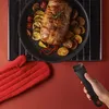 A roasted meat dish with vegetables and potatoes in a pan, with a red oven mitt and a pan handle. Produktbild-Vorschau