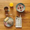 A breakfast setting on a wooden table with a bowl of oatmeal, a glass of orange juice, a cup of coffee, and a plate with bread, cheese, and ham. Produktbild-Vorschau