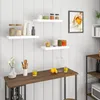 A kitchen scene with white paneled walls, featuring several white floating shelves displaying various kitchen items, and a wooden countertop with more items. Produktbild-Vorschau