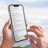 A person is holding an iPhone with a transparent case, displaying the phone's settings menu. Produktbild-Vorschau