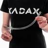 A person wearing a black t-shirt with the KADAX logo is holding a clear plastic tube. Produktbild-Vorschau