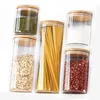 A set of five glass storage jars with bamboo lids, filled with different food items like pasta, beans, and oats. Produktbild-Vorschau