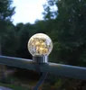 A solar-powered light globe attached to a railing, with trees in the background. Produktbild-Vorschau