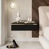 A modern bedroom scene featuring a black floating nightstand with gold accents, a bust sculpture, and toiletries. Produktbild-Vorschau