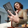 A woman sitting in a chair outdoors, holding a phone case with a ring holder. Anteprima dell’immagine prodotto