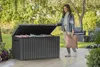 A woman is putting a pillow into a large outdoor storage box in a garden setting. Produktbild-Vorschau