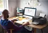 A man is working at a desk with a computer and printer. Produktbild-Vorschau