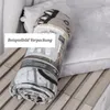 A rolled-up fleece blanket in its packaging, placed on a wooden surface with a blurred background of a light-colored fabric. Produktbild-Vorschau