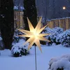 A lit star decoration stands in a snowy garden at dusk, with fairy lights in the background. Produktbild-Vorschau