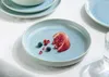 A light blue plate with blueberries and a slice of pomegranate on a white tablecloth. Náhľad obrázku produktu