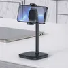 A black smartphone stand is shown on a white desk, with a tablet in the background. Produktbild-Vorschau