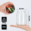 A hand holds a jar filled with tomatoes and cucumbers, next to an empty glass jar with dimensions and weight information. Anteprima dell’immagine prodotto