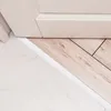A close-up view of a floor transition between marble and wood flooring, with a white transition strip. Produktbild-Vorschau