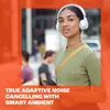 A woman wearing white headphones and a green sweater is looking at her phone while walking outside. Voir les images du produit