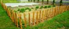 A garden fence made of wooden stakes and wire encloses a garden bed with plants and a covered area. Produktbild-Vorschau
