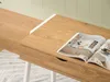 A close-up of a wooden desk with a magazine open on it, set against a light green wall and wooden floor. Voir les images du produit