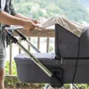 A person is adjusting a sun cover on a baby stroller outdoors. Produktbild-Vorschau