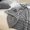 A close-up view of a soft, textured gray blanket draped over a white bed. A matching pillow is visible in the background. Produktbild-Vorschau