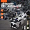 A labeling machine is shown on a wooden table with bottles and a champagne bottle in the background. The machine has labels on it and is ready for use. Náhled obrázku produktu