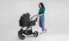 A woman pushing a black baby stroller. Anteprima dell’immagine prodotto