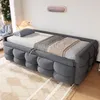 A gray upholstered daybed with a mattress, pillow, and blankets is shown in a room with a patterned rug and a lamp. Produktbild-Vorschau