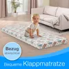 A baby is crawling on a folded mattress in a living room with a sofa in the background. Produktbild-Vorschau