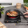 A black induction hob with a frying pan containing chicken and vegetables is shown on a kitchen counter. Produktbild-Vorschau