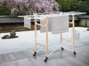 A wooden and white clothes drying rack with towels on it, set in a Japanese-style garden with gravel and rocks. Podgląd zdjęcia produktu