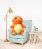 A large orange plush toy resembling Charmander from Pokemon is sitting on a light blue armchair in a room with white walls and a floor lamp. Produktbild-Vorschau