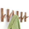 A set of wooden branch-shaped coat hooks mounted on a white wall, with a green jacket hanging on one of the hooks. Náhled obrázku produktu