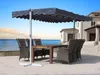 An outdoor dining set with a large umbrella on a patio overlooking the ocean. Produktbild-Vorschau