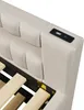 A close-up view of the headboard of a beige upholstered bed frame, showing a built-in USB charging port. Produktbild-Vorschau