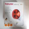 The image shows the packaging of a Beurer infrared lamp. The front of the box displays the product name, brand, and an image of the lamp itself. There is also a lifestyle image of a woman using the lamp. Produktbild-Vorschau