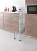 A slim, three-tier metal rolling cart is shown in a modern kitchen setting, positioned between cabinets and next to a countertop with a coffee machine and jars. Produktbild-Vorschau