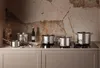 A collection of stainless steel pots and pans arranged on a stovetop against a textured wall. Produktbild-Vorschau