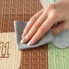A hand is wiping a colorful play mat with a gray cloth. Produktbild-Vorschau