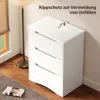 A white chest of drawers with a safety strap attached to the top, placed in a room with a floor lamp and a window. Podgląd zdjęcia produktu