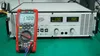 A red and black multimeter is placed in front of a large power supply unit. The multimeter displays '1700' and the power supply has two digital displays showing '170' and '168'. Produktbild-Vorschau