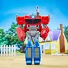 A toy Optimus Prime transformer stands in a yard with a house and fence in the background. A small figure of a boy stands on Optimus Prime's shoulder. Podgląd zdjęcia produktu