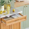 A kitchen island with lemons and kitchenware on top, and open drawers revealing folded cloths. Produktbild-Vorschau